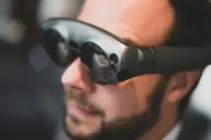 A man wearing futuristic augmented reality (AR) glasses, reflecting a digital interface in his lenses. The image represents the advancement of AR technology in modern applications.
