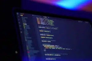 laptop screen displaying JavaScript code in a dark-themed code editor, illuminated by a vibrant blue and purple background.
